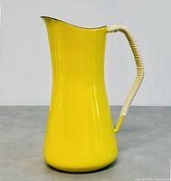 Front and side view of the 7-inch tall yellow enamel pitcher with white wrapped handle, smooth vibrant finish, and curved pouring spout.