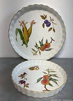 Photo showing two Royal Worcester Evesham pie/baking dishes, one smaller and one larger, both with scalloped edges and hand-painted fruit and corn motifs with gold trim.