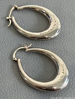 Pair of oval hoop earrings laid flat on grey textured surface.