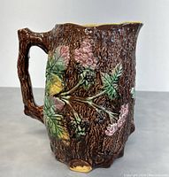 Side view showing bark texture, detailed leaves, berries, and branch-like handle of the pitcher.