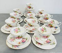 Overall view of 12 teacups with matching saucers and 11 dessert plates in floral pattern and gold trim.