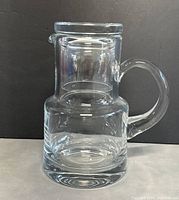 Clear glass bedside water carafe with handle and thick base, viewed from front.