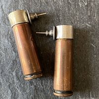 Pair of copper tube earrings laid on a slate background, showing sterling silver caps, posts, and copper tubes measuring approximately 1 3/4 inches.