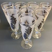 Front angle view of seven out of eight frosted stemmed beer glasses arranged in a cluster, showing silver leaf designs on each glass.