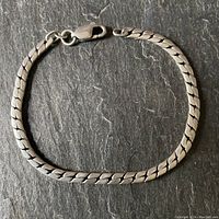 Full view of the men's herringbone link bracelet laid flat on a dark textured surface.