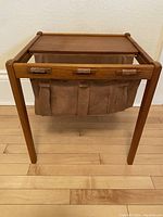 Front view of the teak side table showing the wood frame and attached brown suede magazine pouch with strap details.