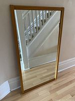Full view of the mirror leaning against the wall showing its size, frame thickness and reflective glass surface.
