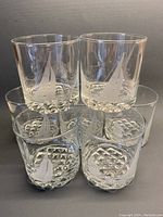 Front view of stacked set of 8 etched sailboat lowball glasses showing different sailboat designs and textured square bottoms reflecting light.