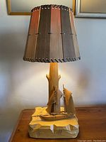 Full view of the wooden lamp with carved sailboat base and original wooden shade illuminated.