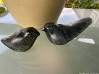 Pair of small soapstone bird sculptures together on glass surface in natural light.