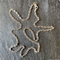 Full view of sterling silver anchor style chain arranged on a dark surface