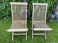 Two folding teak slatted chairs side by side on lawn