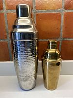 Front view of two cocktail shakers together showing size and finish difference, tall hammered chrome on left, smaller copper color on right.