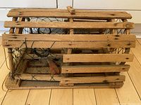 Side view of small wooden lobster trap showing rectangular shape, wooden slats, and green wire mesh construction.