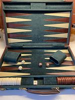 Backgammon board opened showing felt playing surface with brown and cream triangular points, cinnamon and cream checkers, two felt dice cups, and dice placed on the board.