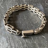 Bracelet laid in a coiled position showing its chunky linked double chain design, polished silver with slight vintage patina.