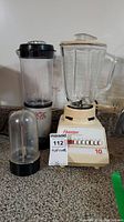 Front view of Osterizer Sunbeam blender and Magic Bullet blender on counter showing the two blending units, accessories, and control buttons.