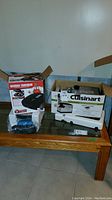 Photo of both boxed items on a wooden table showing the Cuisinart meat grinder box and George Foreman Champ Grill box side by side.