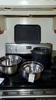 Two stainless steel mixing bowls nested together on stove with black metal pot and oven tray behind them.