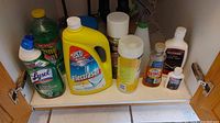 Photo showing assorted cleaning supply bottles under a kitchen cabinet, including Lysol, Electrasol, Murphy Oil Soap, and others.