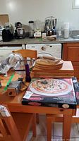 Wide angle photo showing lot contents on table and kitchen counter, includes cutting boards, grinder, rolling pin, pizza baking stone in box, and additional kitchen appliances in background.