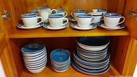 Eight cups with matching saucers arranged on shelf with stacked bowls and plates below