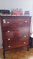 Front view of the dark stained wood dresser showing four drawers with shell-shaped brass handles and items on top.
