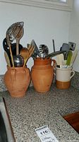 Three ceramic jars holding various used kitchen utensils, on a kitchen counter under a window