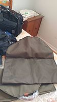 Image of unfolded brown/olive fabric suit bag placed open on table showing interior fabric and construction detail.