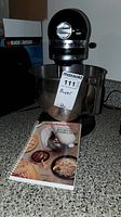 Photo of the KitchenAid stand mixer with stainless steel bowl and the recipe and instruction booklet in front on a countertop.