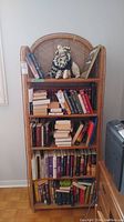 Full front view of the tall wicker shelving unit filled with books and decorative items, demonstrating size and design.