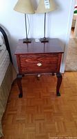 Front view of the wooden side table showing the drawer and decorative handle with two lamps on top.