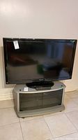Front view of Panasonic Viera flat screen TV on grey TV stand with remote control placed on stand.