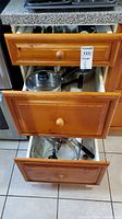 Open view of three wooden kitchen drawers showing pots and utensils inside.