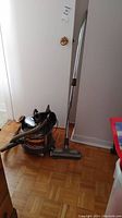 Full view of the vintage Filter Queen vacuum cleaner with attached hose, metal extension wand, and floor nozzle standing upright on hardwood floor.