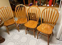 Group of four wooden dining chairs with curved slat backs, light wood finish, placed on tiled floor.
