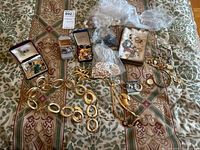 Photo showing assorted costume jewelry items spread on a patterned textile including chain belts, earrings, brooches, necklaces, and packaging materials.