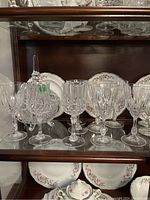 Crystal and glass stemware on a shelf with decorative plates behind