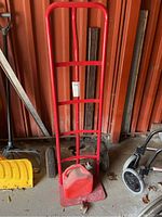 Photo showing full red metal hand truck dolly with large black wheels and red gasoline can resting on base plate