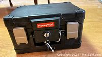 Closed view of the black Honeywell portable safe showing the key lock, red Honeywell logo, and gray side latches.