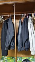 Six men's jackets hung on a closet rod showing various colors including black, navy, gray, and beige.