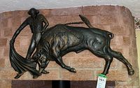 Wide view of metal bull and matador wall sculpture hung on a brick wall.