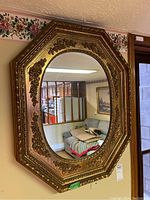 Photo showing the ornate hexagonal wall mirror hanging on a wall in a basement room with floral wallpaper border and furniture reflected in the glass.