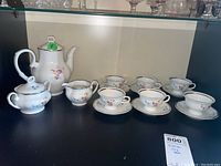 Full view of the tea set including coffee pot, creamer, sugar bowl, six cups and six saucers with floral and gold trim designs on white porcelain.