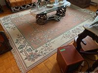 Full view of the rectangular area rug on a wooden parquet floor with visible floral patterns and fringed edges, partially covered by a glass coffee table and living room furniture.