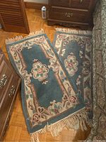 Two small wool rugs laid overlapping. Blue background with floral beige and pastel pattern, fringes on ends, one rug slightly faded.