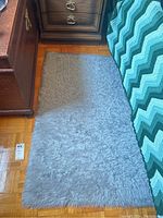 Gray shag rug laid on hardwood floor near furniture and a blanket with green shades pattern.