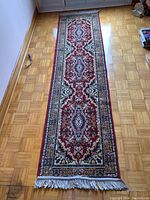Full length view of the machine woven runner rug laid out on parquet flooring showing the central medallion and border pattern with fringe on one end.