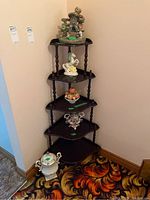 Full view of the five tier wooden corner shelf showing the structure and presence in the corner with decorative items on the shelves.
