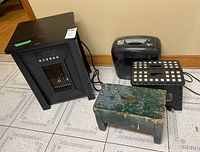 Overall lot showing shredder, electric heater, and two step stools on tiled floor near baseboard